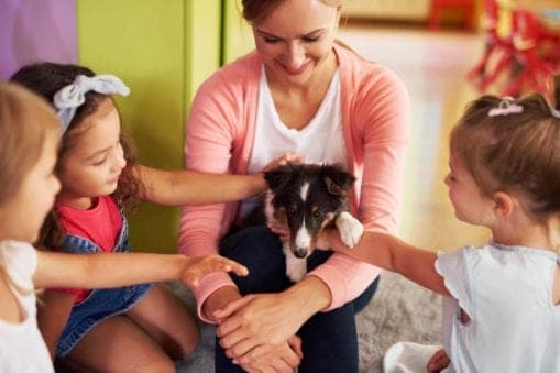 Woman holding puppy while group of young children pet it