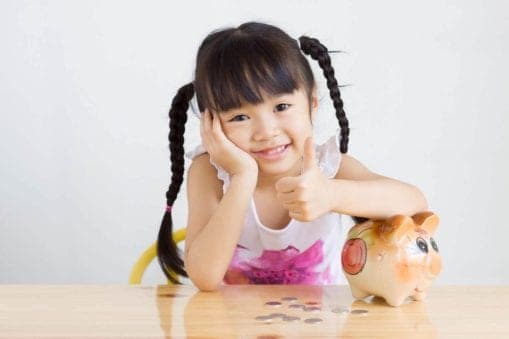 young girl leaning on piggy bank giving thumbs up