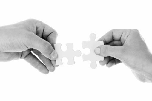 two hands holding puzzle pieces together