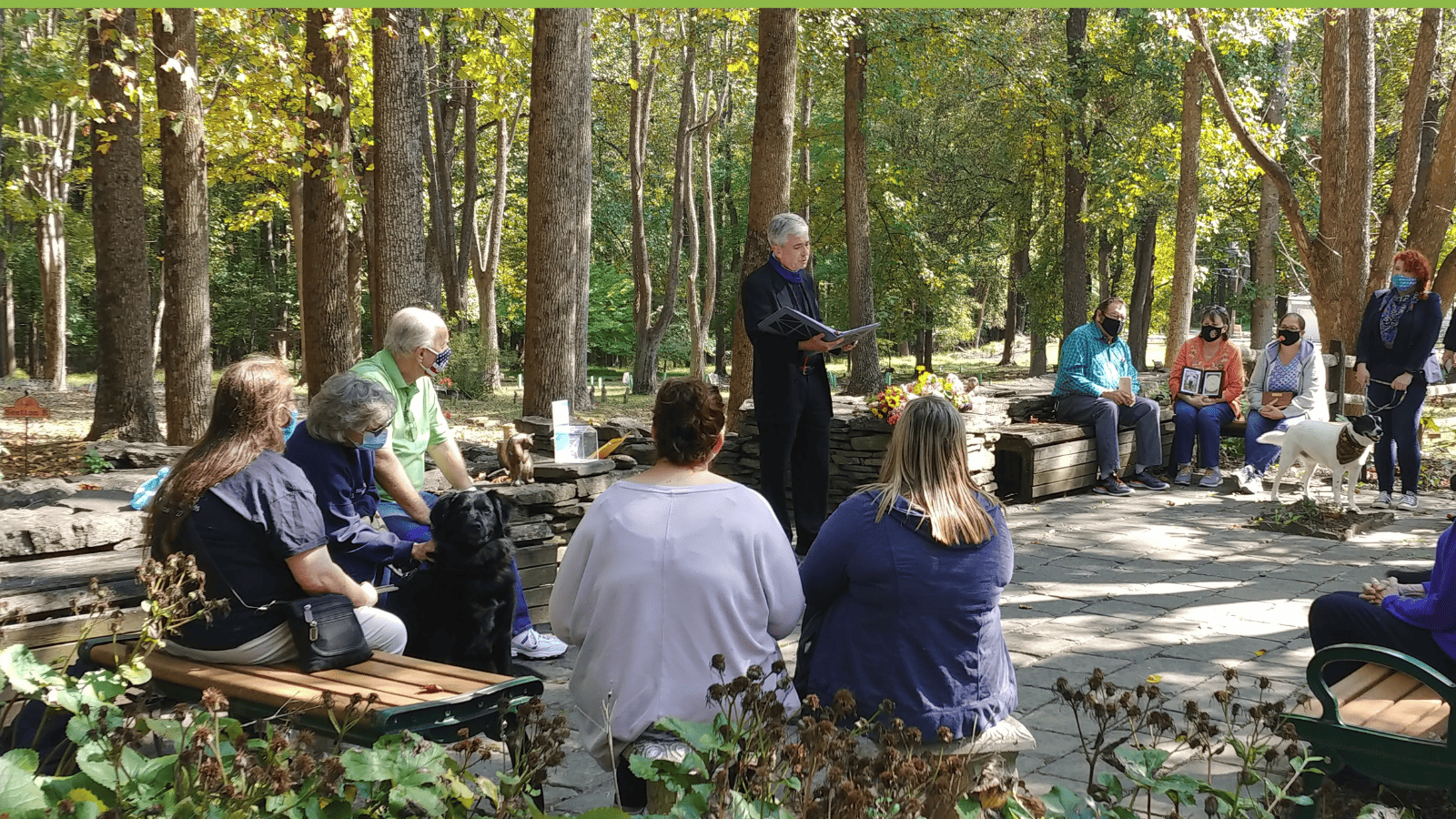 minister readingprayers in the woods surrounded by people and their pets.